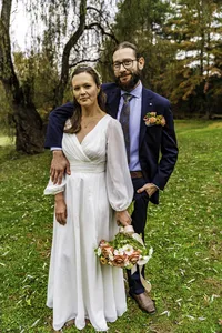 Emily and Josh standing together on a green lawn on their wedding day, her bouquet in hand