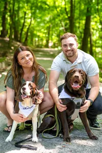 Newly engaged couple crouching on a gravel path in Frick Park with their two dogs
