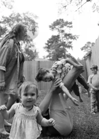 A father holds his son up on his legs while their mother looks down at him and their baby sister looks straight at the camera during their at home family photo session near houston texas