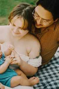 A film photo of a mother and father sitting on a blanket enjoying their baby in the backyard in houston texas