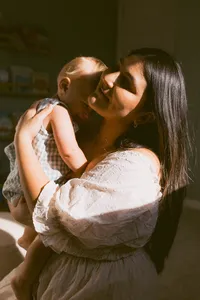 Mother embraces her baby in the sunshine of their home during their at home family photo session near houston texas