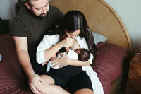 A mother holds her newborn baby and kisses his hand during their at home newborn photos in houston tx
