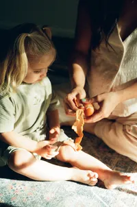 A film photo of a mother peeling an orange for her toddler during her maternity session in her home near houston texas