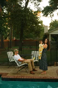 A film photo of a mother and father sitting beside their pool while the mother holds her baby during their at home family photo session near houston texas
