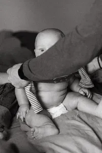 A baby peeks over his fathers arm during an at home newborn session in Houston Texas