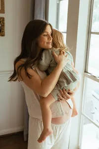 A mother holds her toddler and hugs her tight in her home maternity photo session in houston texas