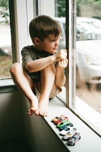 A boy sits with his hot wheels while glancing at the cars outside during an at home family photo session in houston texas