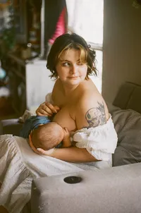 A film photo of a mother nursing her baby in their home and gazing out the window during their at home family photo session near houston texas