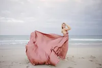 Woman in a flowing pink gown with fabric caught in motion on the beach