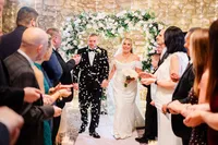 Wedding couple walking down the aisle with heart-shaped white rose wedding arch in the background