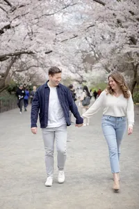 Couple walking hand in hand beneath cherry blossoms during their engagement session