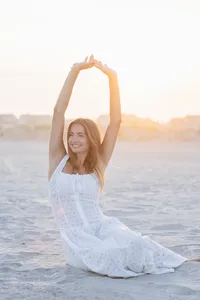 Woman's branding portrait with arms raised at the beach during sunset