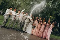 A bride and groom stand with their bridal party as they open a bottle of champagne, by Grand Rapids wedding photography Grace Wan.
