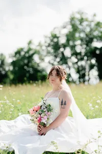 A bride sitting in a field of wildflowers while holding her bouquet during wedding portraits.