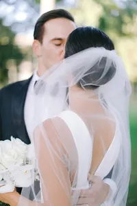 Bride and groom share a close embrace as her veil sweeps across them in a garden setting
