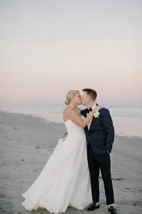 Bride and groom share a kiss on the beach as the sky turns pink at sunset