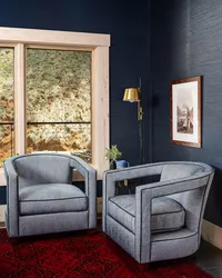 Deep blue grasscloth wallpaper in an Asheville, NC living room, with gray chairs, a gold sconce, and red rug.