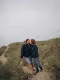 A couple kisses as they walk along a dirt path on the Oregon Coast near Haystack Rock.