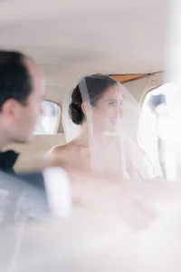Bride laughs beneath her veil while seated in the wedding car
