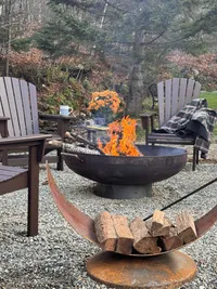 Wood-burning fire pit with flames and stacked firewood at Brookside Retreat