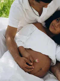 Close up of a pregnant mother lying on her husband's lap, by Michigan maternity photographer Grace Wan.