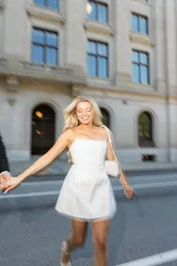 Bride in a short white dress running across a city street in front of a historic stone building