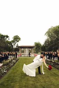 bride walking on ceremony lawn - Photograph of bride in flowing white gown walking across manicured grass with formal gazebo and seated guests in background