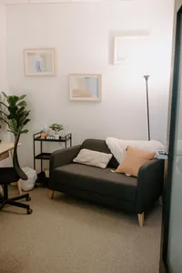 love seat with pillows and blanket that are near a table and chair in therapy office.
