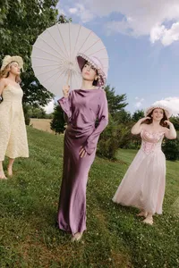 Bridesmaids in pastel dresses and sun hats holding a white parasol in a grassy field at Missem and Ege's wedding