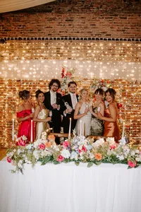 wedding party with colourful floral wedding table centrepiece and floral wedding arch with fairy light backdrop