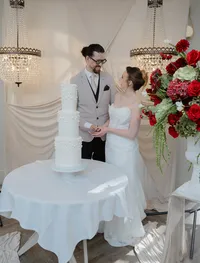 wedding couple cutting cake with a red and burgundy floral arrangement on a plinth