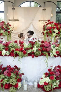 wedding couple sitting amongst red and burgundy wedding flower arrangements