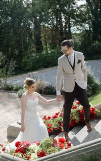 wedding couple climbing outdoor staircase lined with red and burgundy wedding flower arrangements