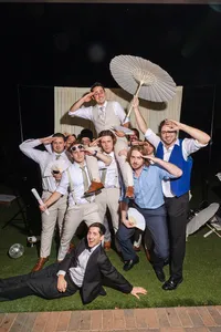 Group of wedding guests posing playfully with parasols and fans in an outdoor photo booth at night, photographed by Dove and Fox