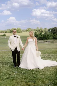 Bride and groom hold hands in a countryside field with fences and rolling hills behind them