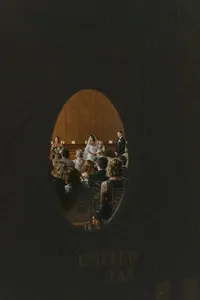 Grace and Jacob's wedding ceremony seen through an oval doorway, with guests seated before a wood-panelled wall, photographed by Dove and Fox
