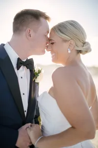 Groom kisses bride's nose on the beach as golden hour light glows around them