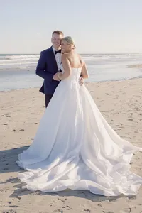 Bride and groom embrace on the beach with ocean waves rolling in behind them