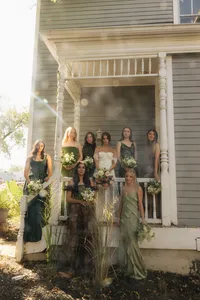 bride with bridesmaids at white portico - Photograph of bride in white gown surrounded by bridesmaids in sage green dresses standing on white columned porch with natural sunlight