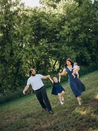 A mother and father swing their daughter as the mother also holds their baby.