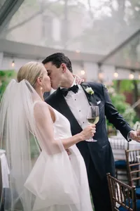 Bride and groom share a kiss while holding wine glasses at a tented reception