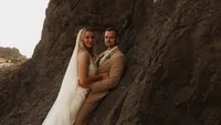 bride and groom under rocky cliff - Wedding videography still of couple embracing together beneath large natural rock formation or cave overhang