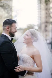 Bride and groom smile at each other on a city street with her veil catching the light