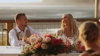 Wedding videography still of couple seated together at dining table with colorful floral centerpiece between them