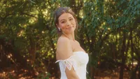 Wedding videography still of bride in white dress standing in wooded outdoor location
