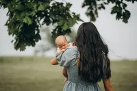 A mother walks with her back to the camera as she holds her newborn up to her shoulder, by Grand Rapids family photographer Grace Wan.