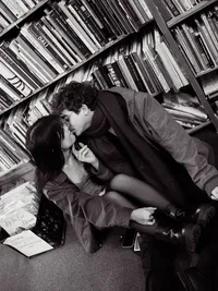 Black and white couples photo of a man and woman kissing while sitting in front of a bookshelf.