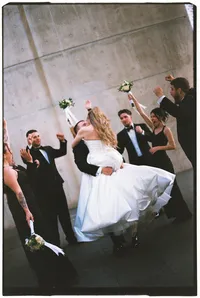 Destination wedding photography of a groom holding up his bride while their bridal party celebrates in the back.