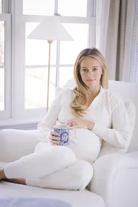 Pregnant woman's branding portrait in cream loungewear holding a coffee mug