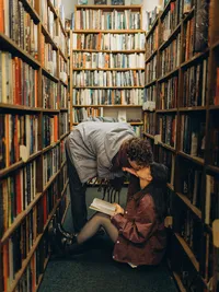Grand Rapids engagement photography of a man kissing his fiancé as she sits on the ground with a book.